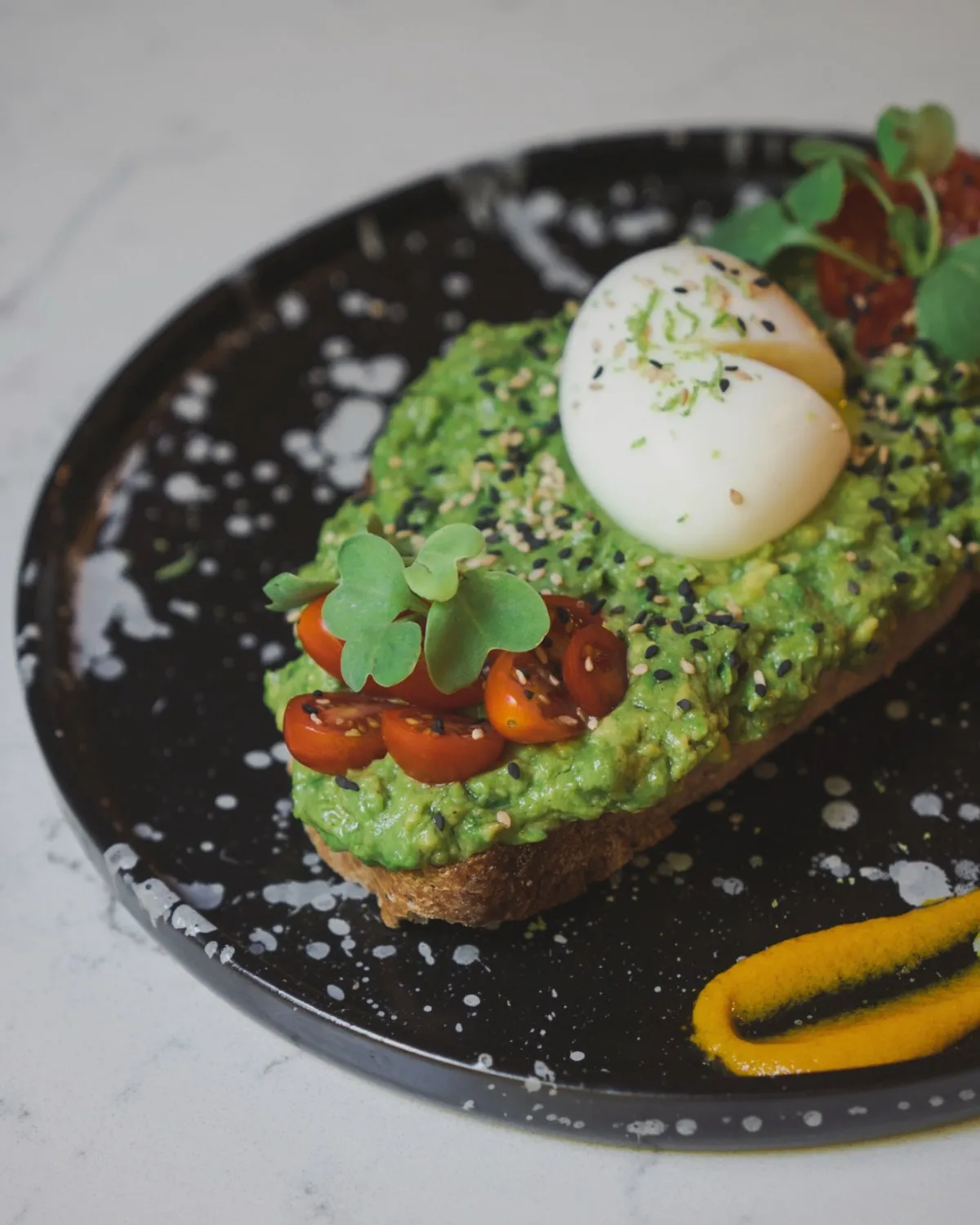 Avocado toast con huevo, tomates cherry y brotes, sobre plato negro