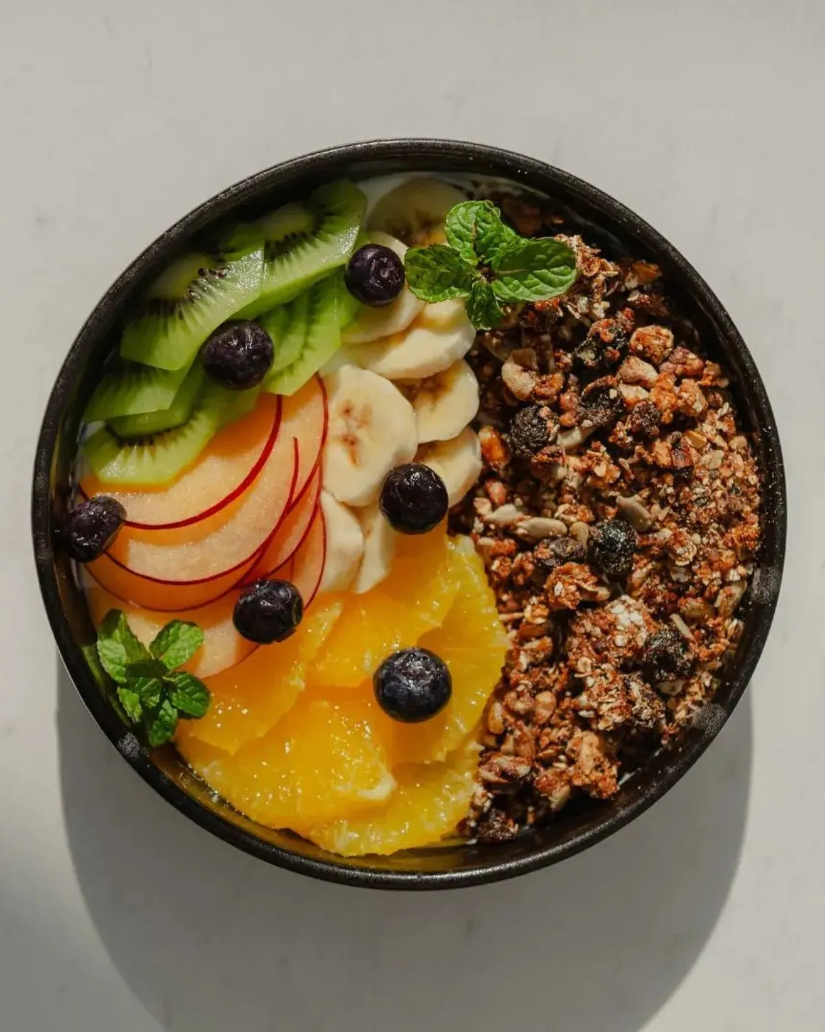 Bowl de frutas de estación con granola, arándanos y menta, visto desde arriba